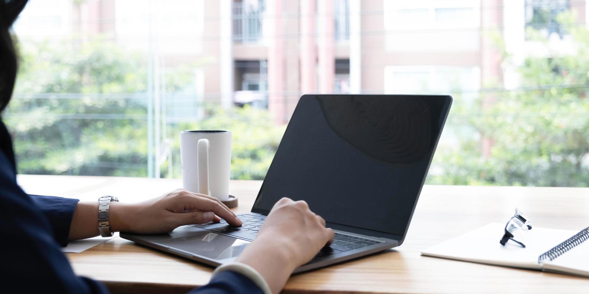 Over shoulder close up view of female hands typing on laptop with mock-up screen on office desk with stationery photo