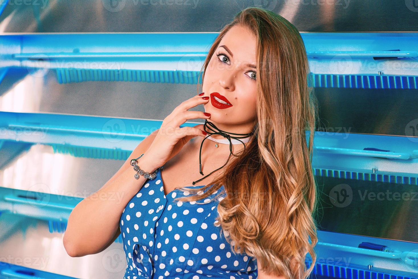 portrait of beautiful attractive pretty long haired young woman in polka-dot blue dress with stylish make up in pin up style on the blue background. Femininity, womanhood, fashion concept photo