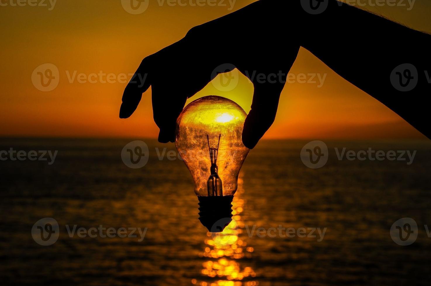 Hand holding lightbulb at sunset photo