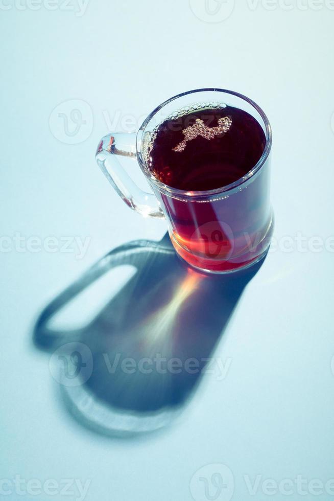 Hot tea in a glass cup with hard shadow on blue background. photo
