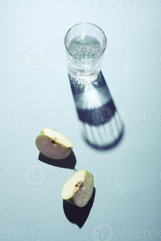Glass of water and pieces of apple on blue background. photo