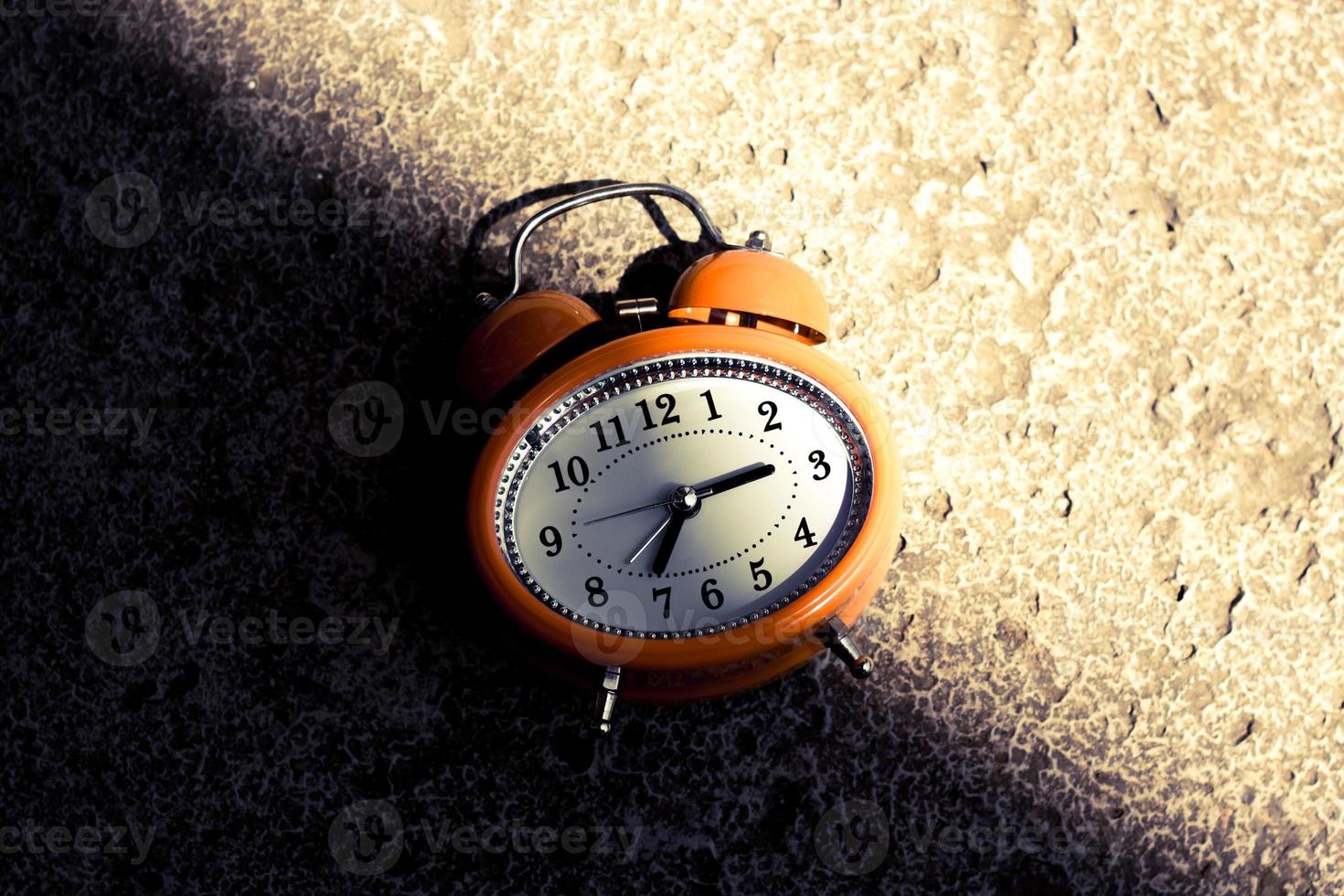 Vintage style orange alarm clock under the bright light and dark shadow. photo