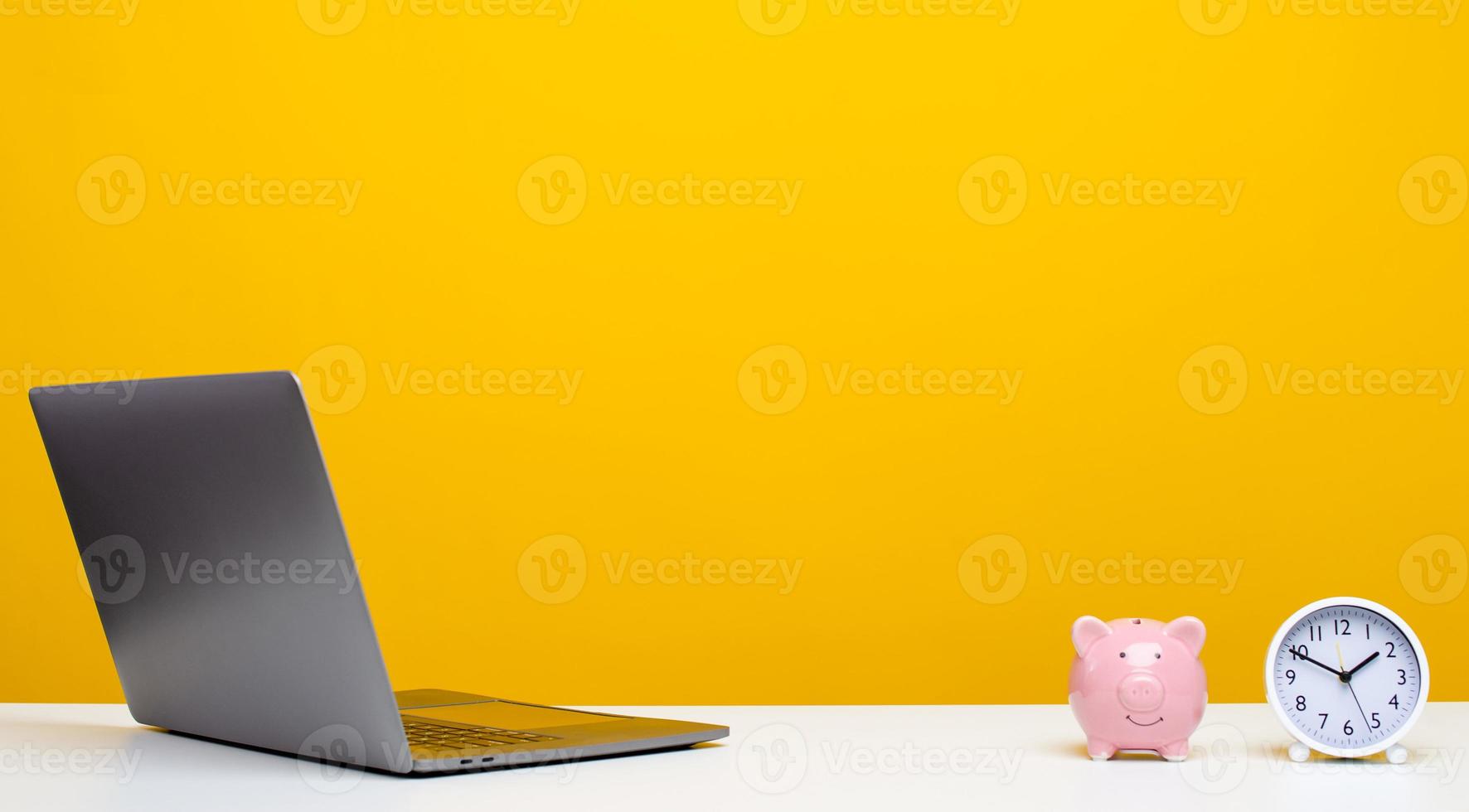 Desk with laptop with clock and piggy bank, designer workspace with copy space. photo