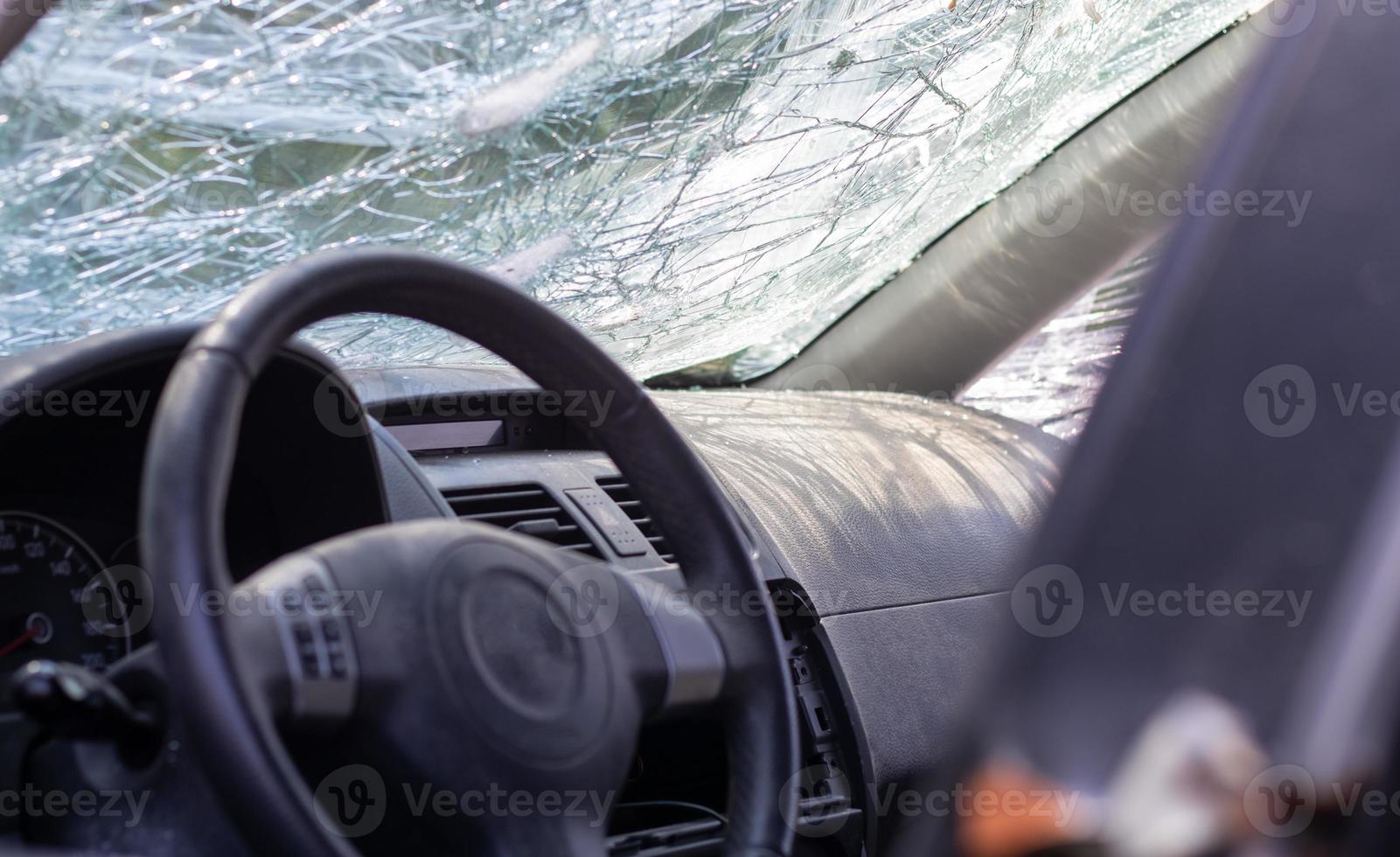 primer plano del volante de un coche después de un accidente. las bolsas de aire del conductor no se desplegaron. enfoque suave. parabrisas roto con volante. interior del vehiculo salpicadero y volante negros. foto