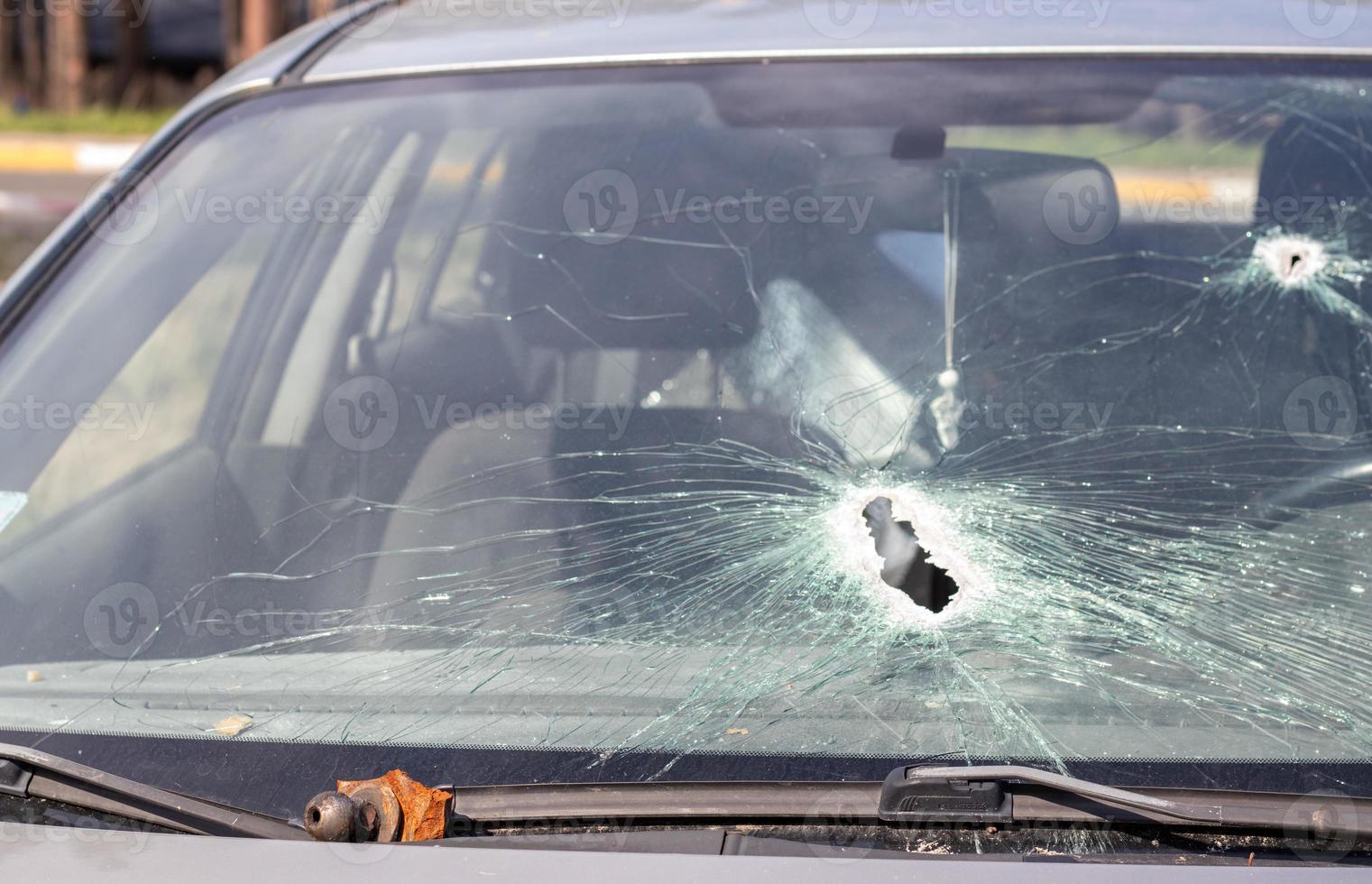 agujeros en el parabrisas del coche, fue disparado con un arma de fuego. agujeros de bala. rompa el parabrisas del coche, el coche roto y dañado. la bala hizo un agujero agrietado en el vidrio. foto