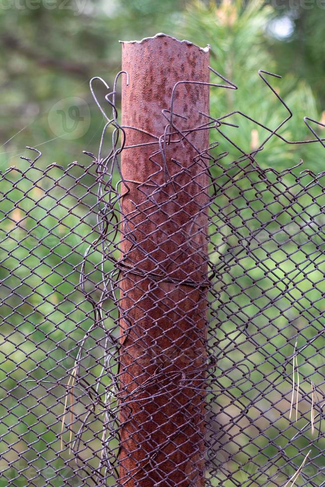 Malla vieja jaula irregular en el jardín y un poste oxidado con hierba verde como fondo. valla metálica con malla de alambre. valla metálica de malla de hierro de acero. fondo abstracto. copie el espacio foto