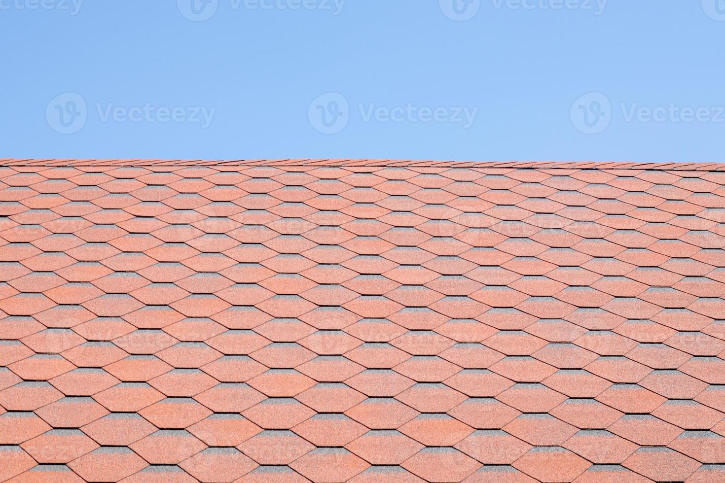 New roof with red shingles against the blue sky. High quality photo. Tiles on the roof of the house. Use to advertise roof fabrication and maintenance. Spotted texture. Affordable roofing. photo