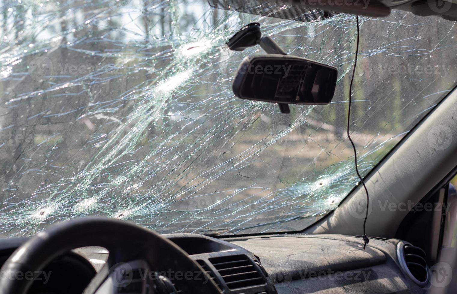 Broken windshield of a car from a bullet, from a shot from a firearm, view from the inside of the cabin. Damaged glass with traces of an oncoming stone on the road. Interior view of the car. photo