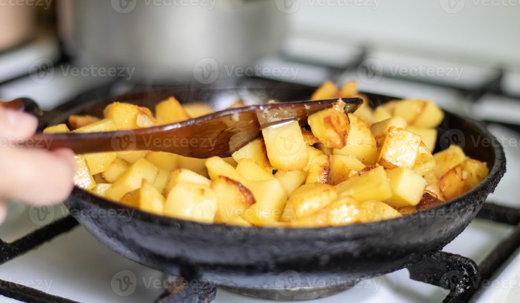 Roasting fresh potatoes in a cast iron skillet with sunflower oil. A view of a stovetop with a frying pan filled with golden fried potatoes in a real kitchen. Food cooked in a homemade frying pan. photo
