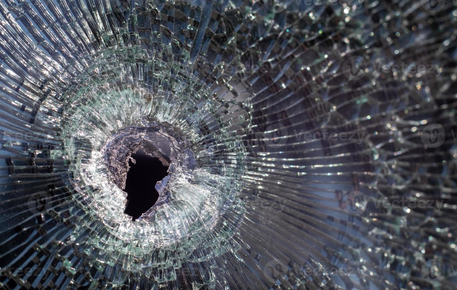 Bullet hole in glass with cracks, real bullet hole close-up. Authentic shot. The bullet made a cracked hole in the windshield of a car or a window glass shattered as a result of an accident. photo