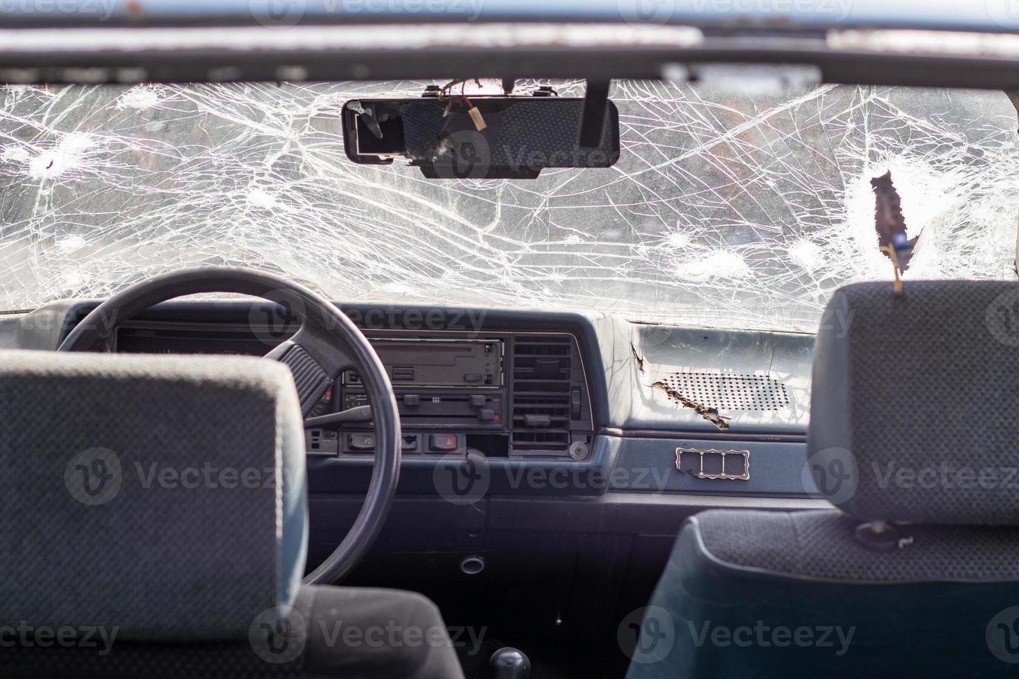 Broken windshield of a car from a bullet, from a shot from a firearm, view from the inside of the cabin. Damaged glass with traces of an oncoming stone on the road. Interior view of the car. photo