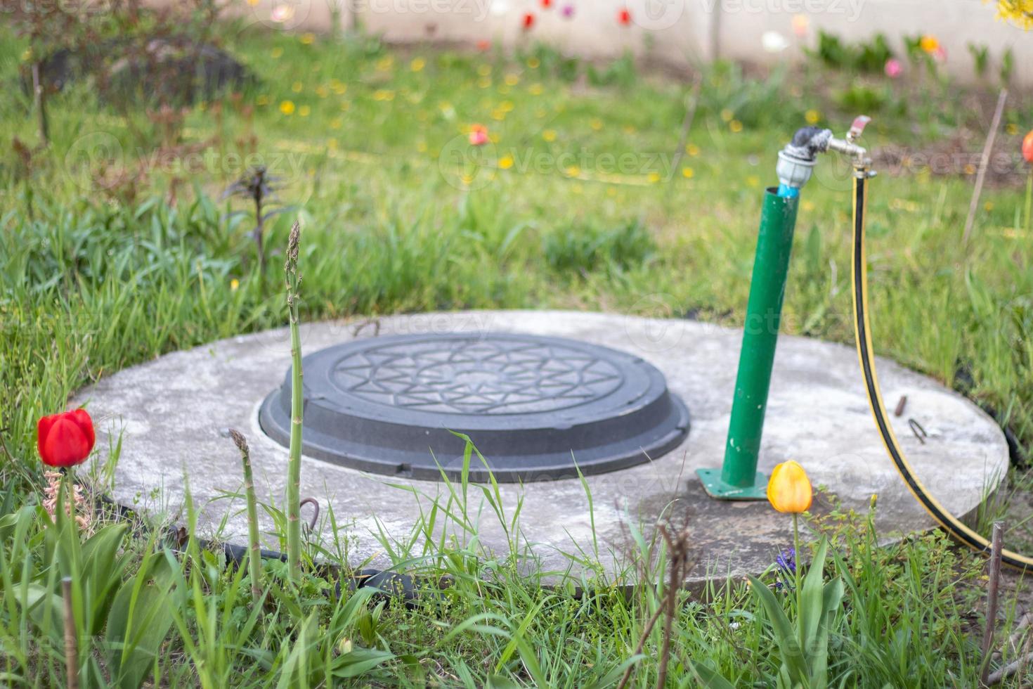 Plumbing, water pump from a well. An outside water faucet with a yellow garden hose attached to it. Irrigation water pumping system for agriculture. Hose in the garden for watering, sunny summer day. photo