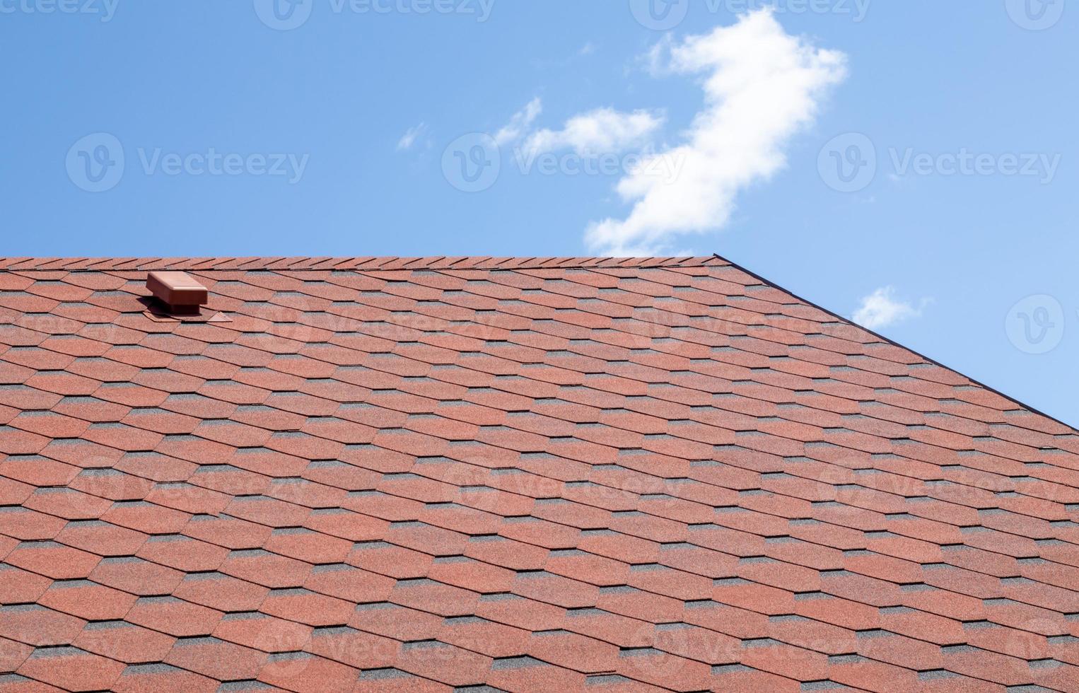 New roof with red shingles against the blue sky. High quality photo. Tiles on the roof of the house. Use to advertise roof fabrication and maintenance. Spotted texture. Affordable roofing. photo