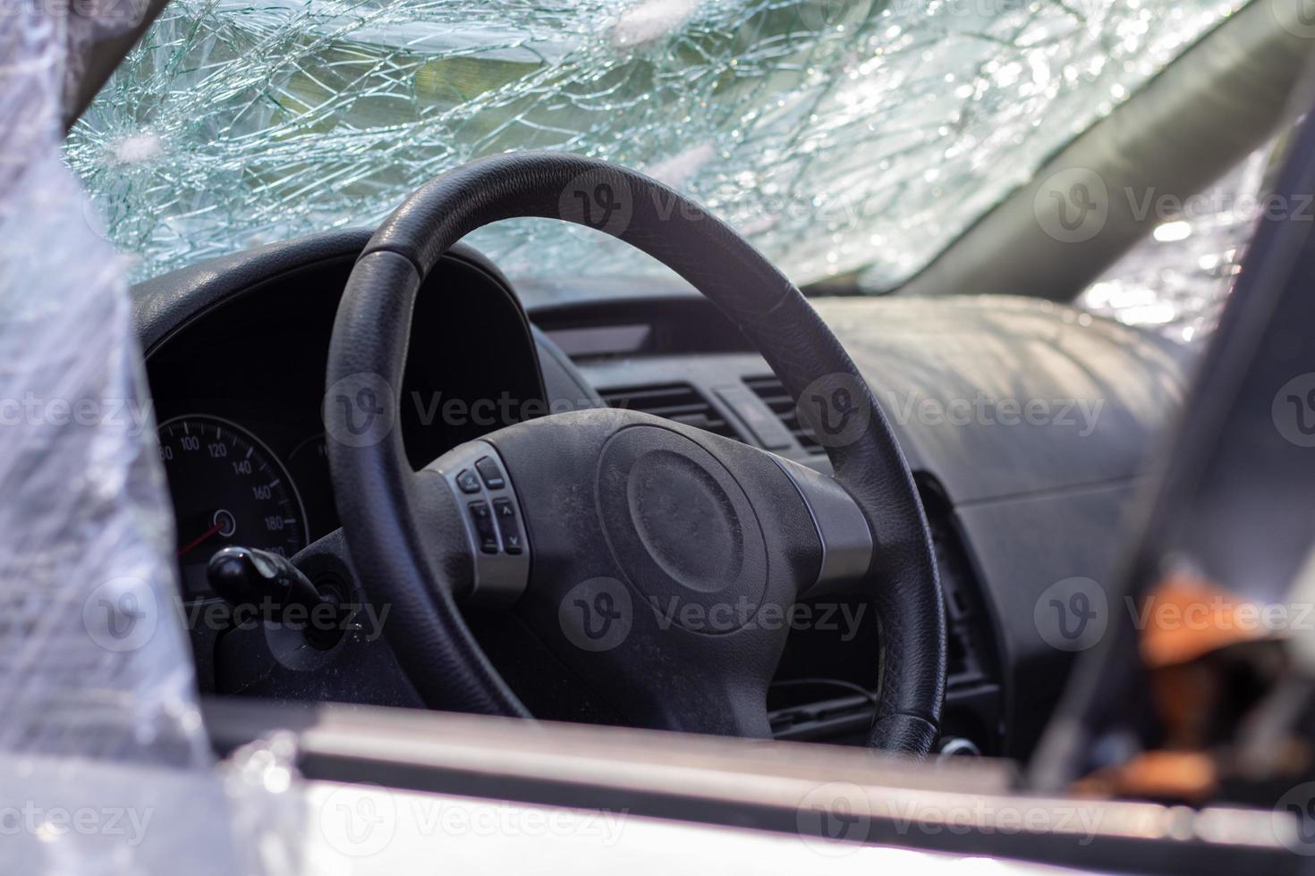 el volante de un coche después de un accidente. las bolsas de aire del conductor no se desplegaron. vista desde la ventana lateral izquierda. parabrisas roto con volante. Salpicadero y volante negros polvorientos. foto