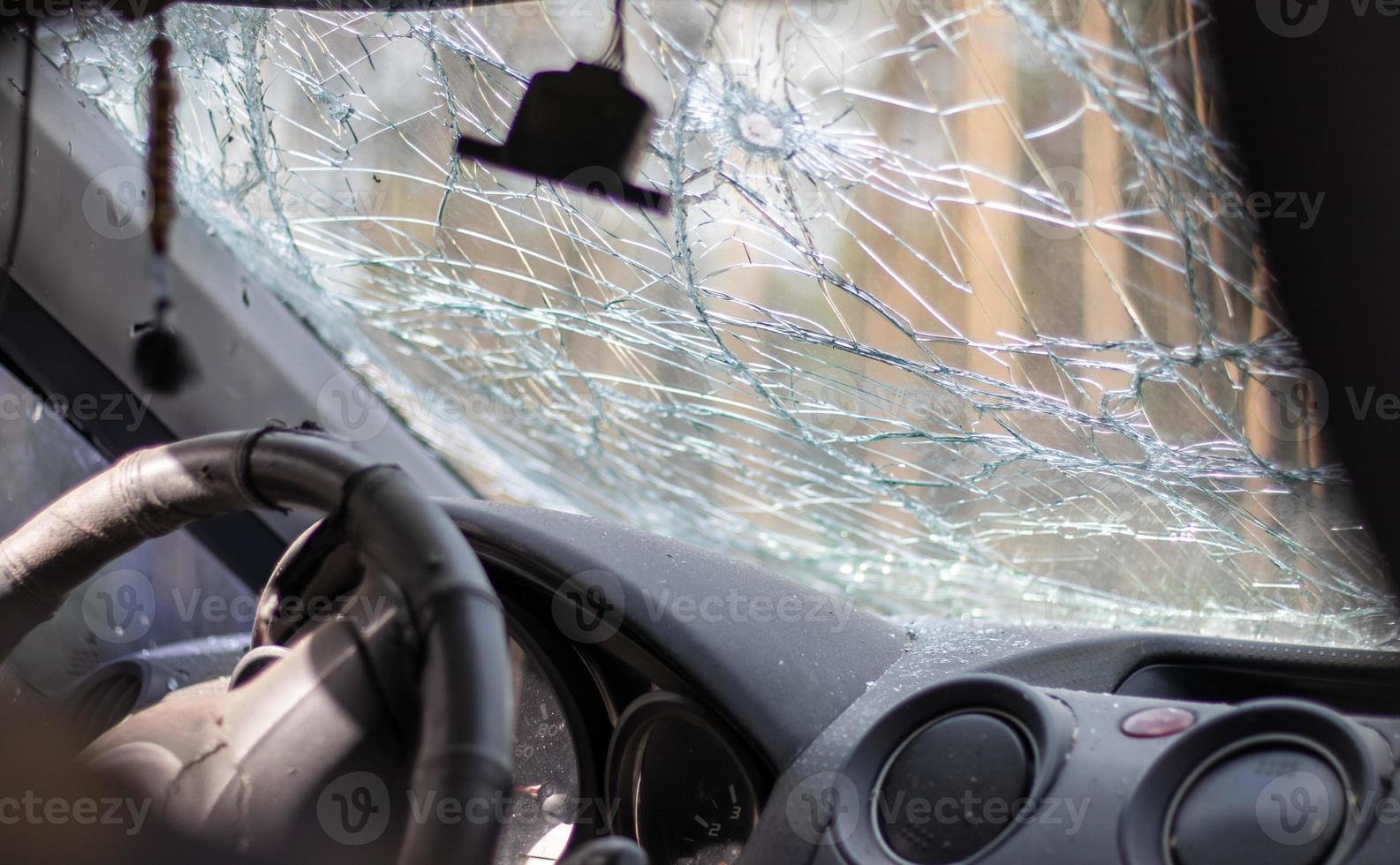 Broken windshield of a car from a bullet, from a shot from a firearm, view from the inside of the cabin. Damaged glass with traces of an oncoming stone on the road. Interior view of the car. photo