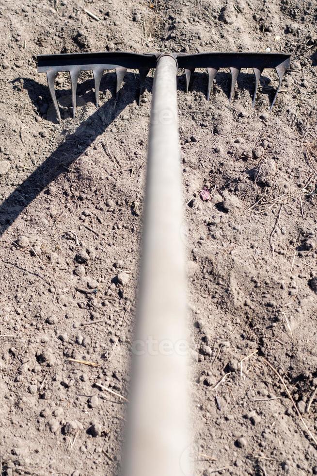 Close up photo of a garden rake on a bed. Old black metal rake on dry soil, in the garden. Spring cleaning. Selective focus. Yard area cleaning.