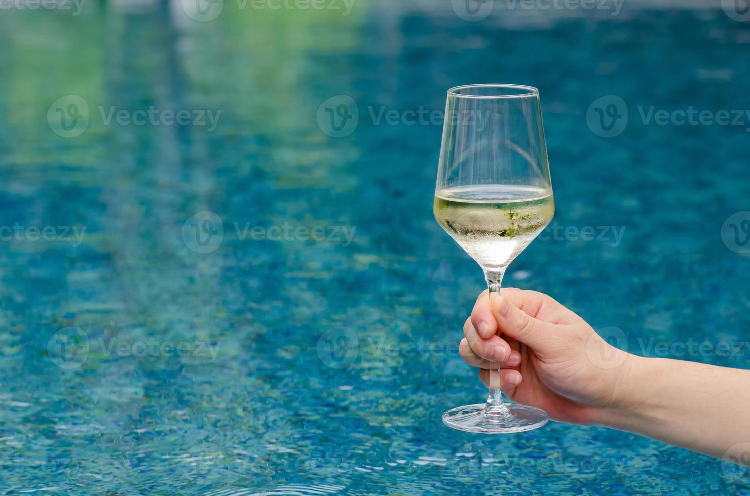mano sosteniendo una copa de vino blanco con fondo de piscina. concepto de bebida de vacaciones y verano. foto