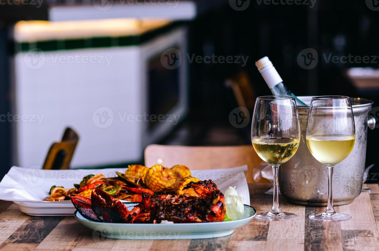 Two glasses of white wine on the table with a bottle in wine chiller bucket and seafood dish for a couple dining. photo