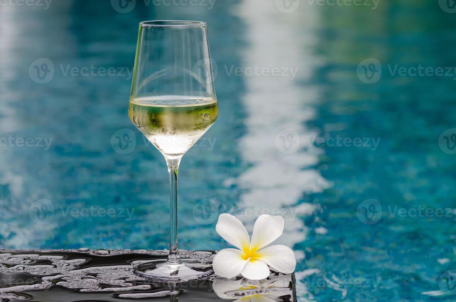 una copa de vino blanco con flor de frangipani puesta en la piscina. concepto de bebida de vacaciones y verano. foto