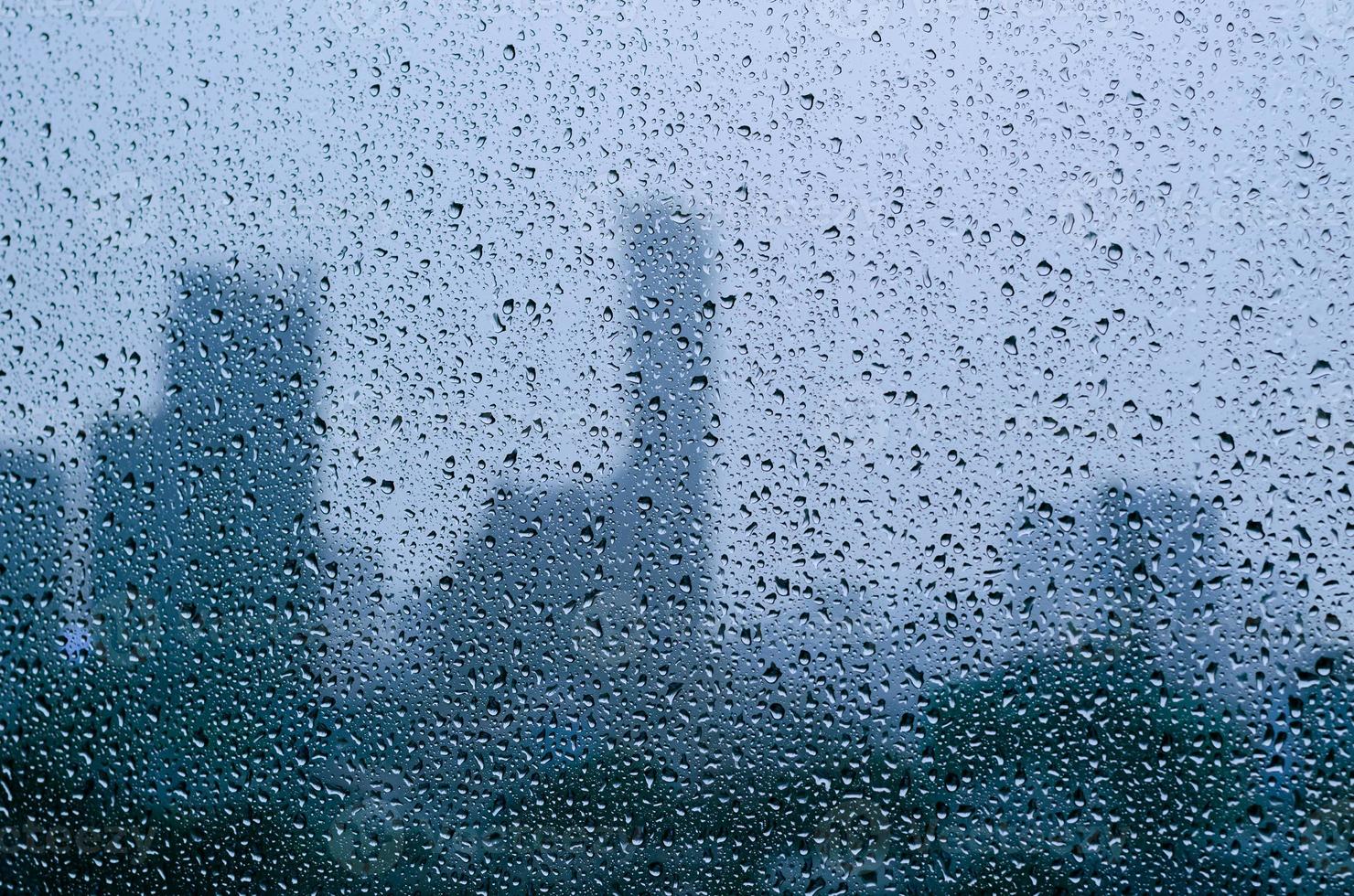 Rain drop on glass window at day time in monsoon season with blurred city buildings background. photo