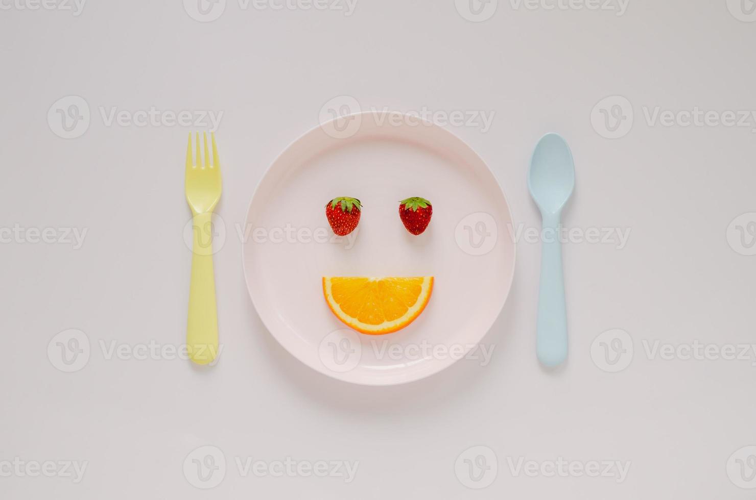 Strawberries  and cutting fresh orange fruit set as happy face on pink plate with fork and spoon on pastel background. Minimal creative healthy diet food concept. photo