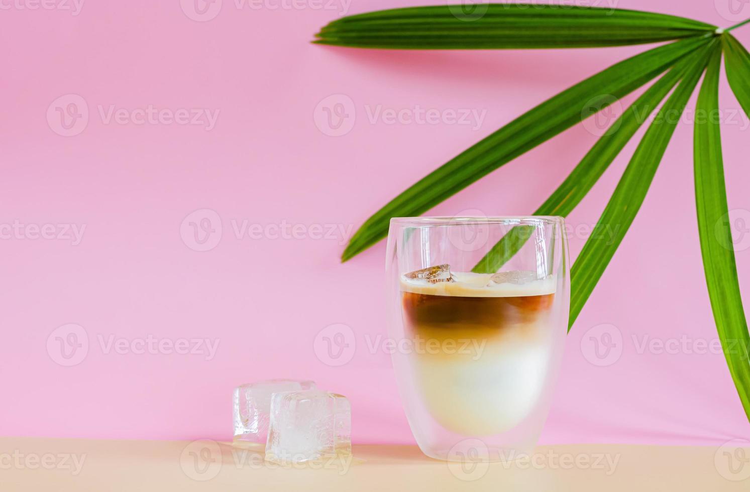 A glass that cover with some vapour of coffee mixing milk on brown and pink background photo