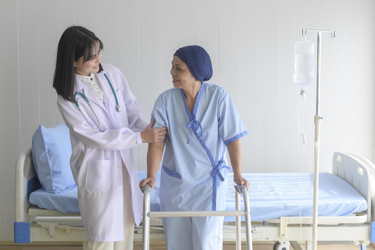 médico que ayuda a una paciente con cáncer que usa pañuelo en la cabeza con un andador en el hospital, atención médica y concepto médico foto