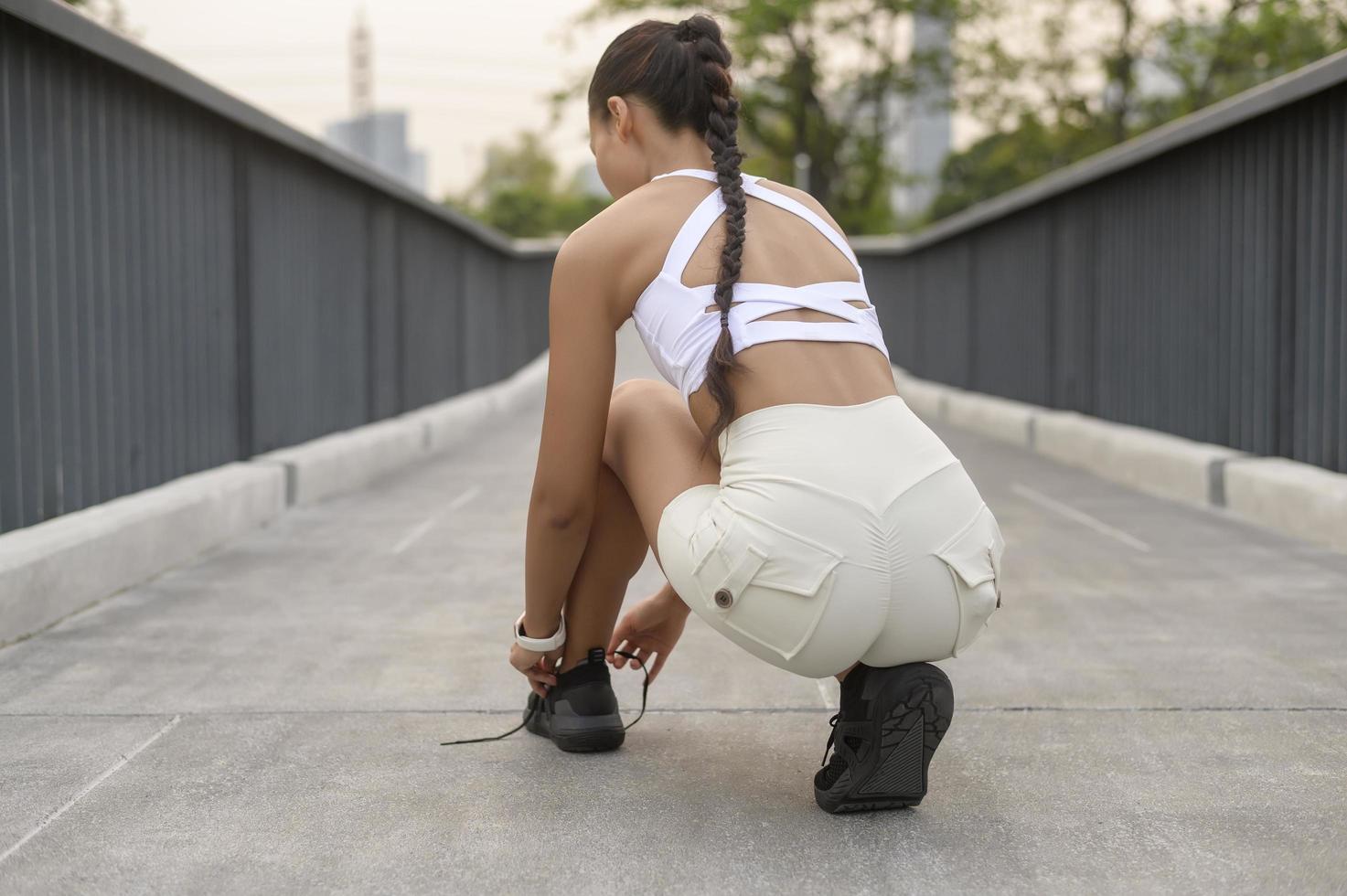 mujer joven fitness en ropa deportiva atando cordones de zapatos en el parque de la ciudad, saludable y estilos de vida. foto