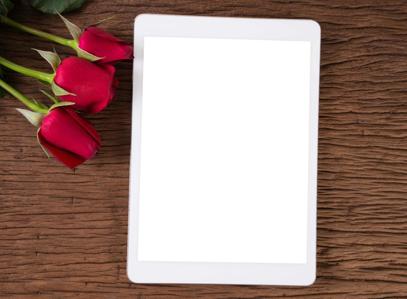 Tablet computer and red rose on old wooden background photo