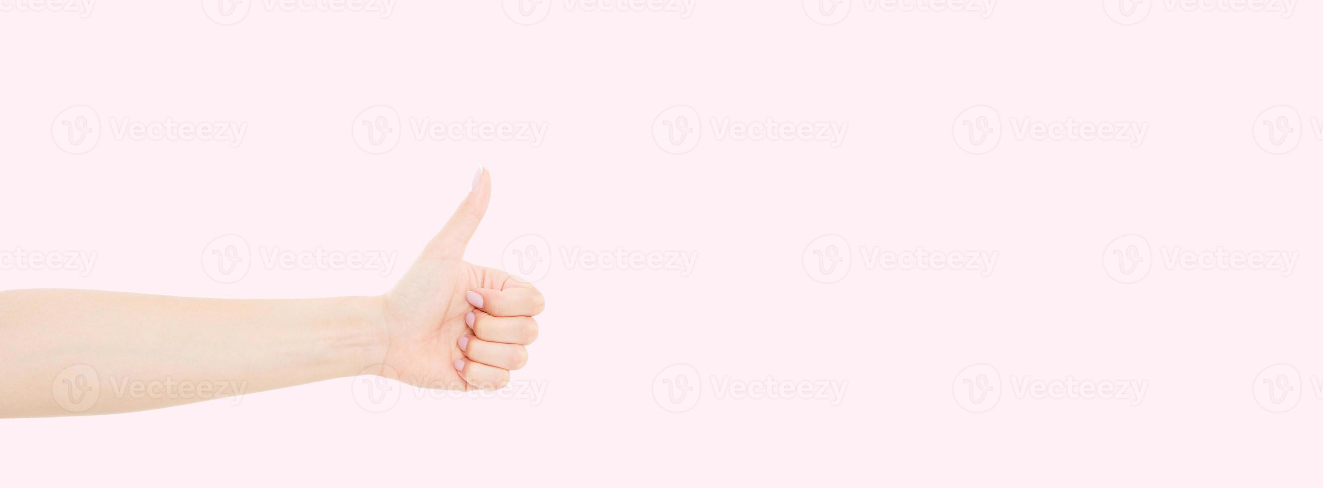 woman with beautiful manicure on fingernails holding hand in gesture of likeness giving thumb up. Close up horizontal color image of human female one hand isolated on pink background photo