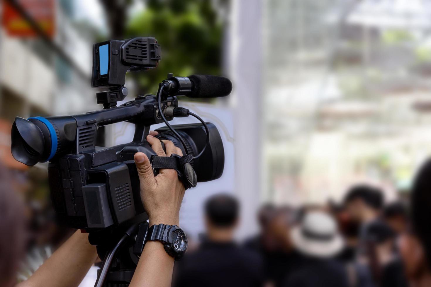 hand holding a video camera with a lot of people  blurred background photo