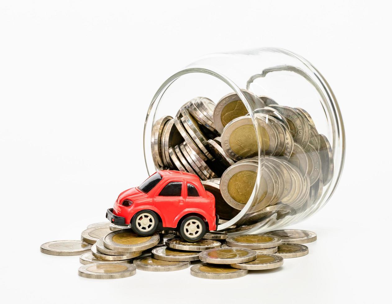 monedas en botella de vidrio y coche rojo sobre fondo blanco, ahorro empresarial y concepto de inversión foto