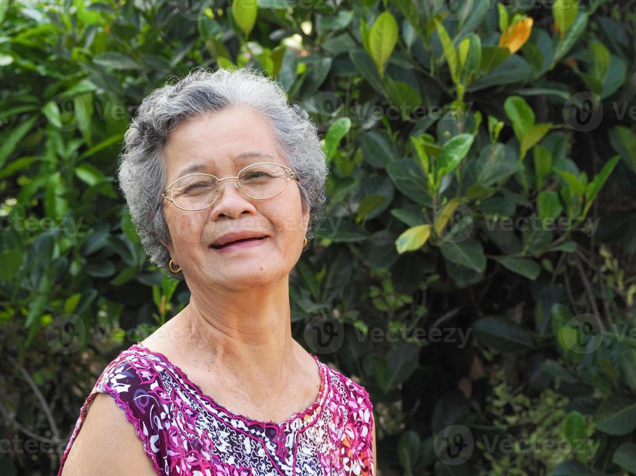 retrato de una anciana con anteojos mirando a la cámara mientras está de pie en un jardín foto