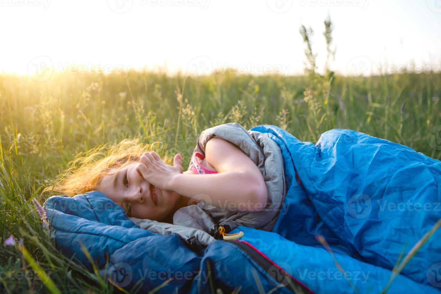 The girl is dissatisfied with scratching mosquito bites, child sleeps in a sleeping bag on the grass in a camping trip. Eco-friendly outdoor recreation, summer time. Sleep disturbance, repellent. photo