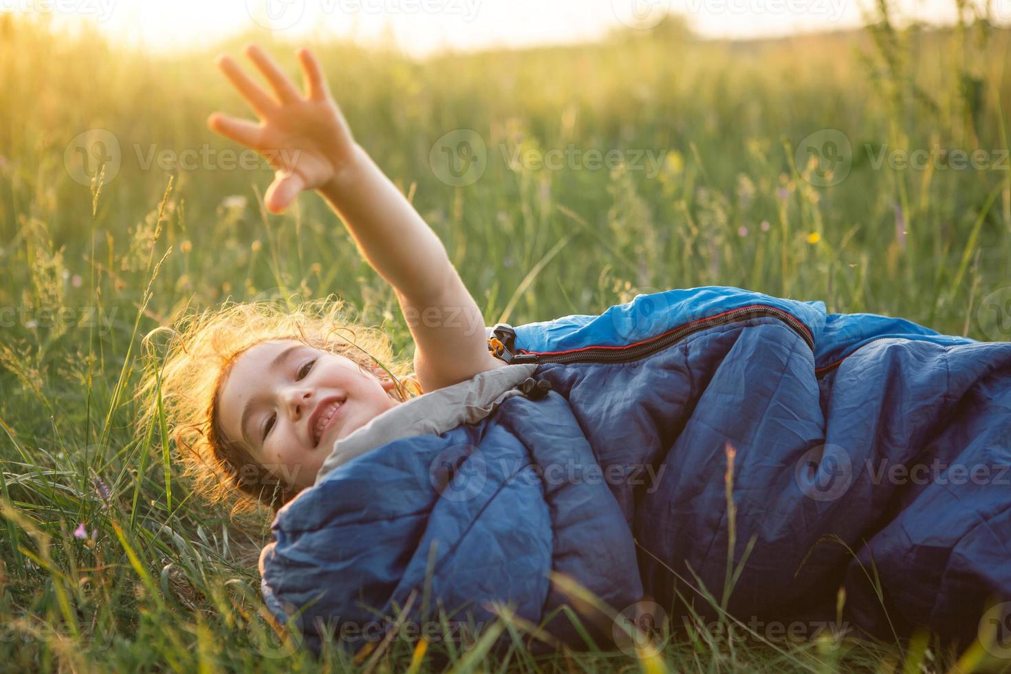 A child sleeps in a sleeping bag on the grass in a camping trip - eco-friendly outdoor recreation, healthy lifestyle, summer time. Sweet and peaceful sleep. Mosquito bites, repellent. photo