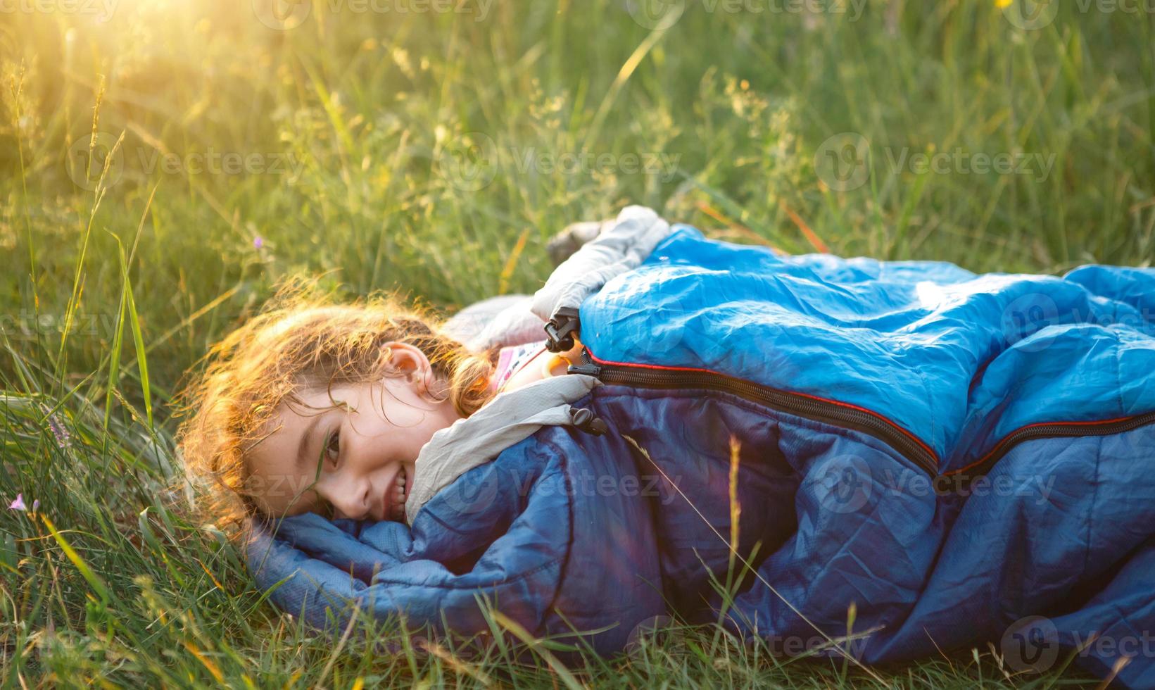 A child sleeps in a sleeping bag on the grass in a camping trip - eco-friendly outdoor recreation, healthy lifestyle, summer time. Sweet and peaceful sleep. Mosquito bites, repellent. photo