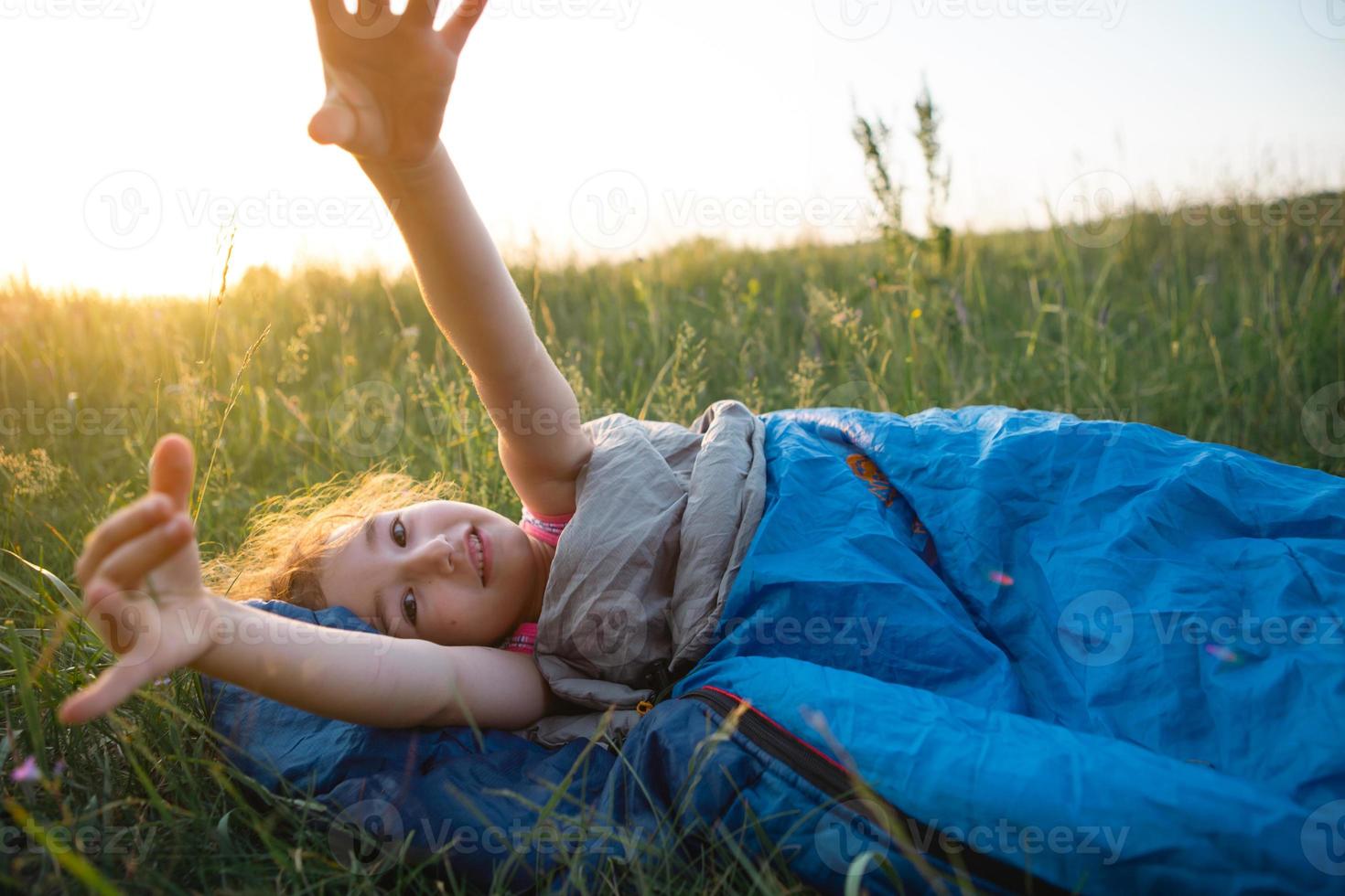 A child sleeps in a sleeping bag on the grass in a camping trip - eco-friendly outdoor recreation, healthy lifestyle, summer time. Sweet and peaceful sleep. Mosquito bites, repellent. photo