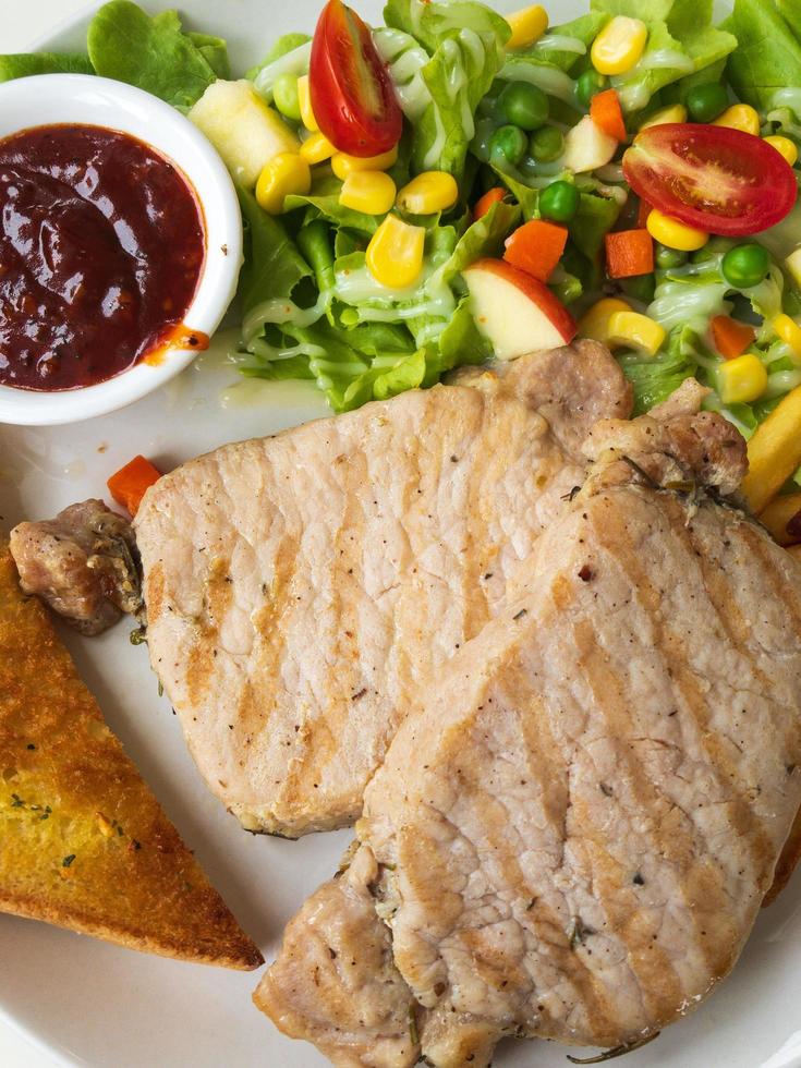 closeup of pork steak with salad, bread and barbecue sauce on a white plate photo