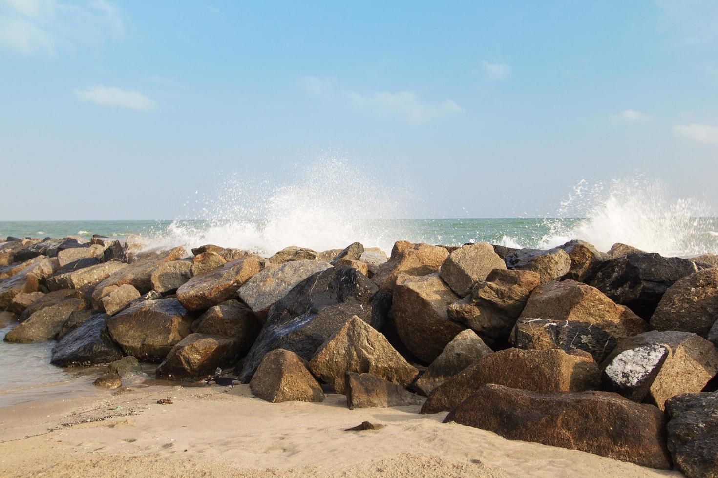 Rocky coastline with long waves lapping with sand and blue sky. photo