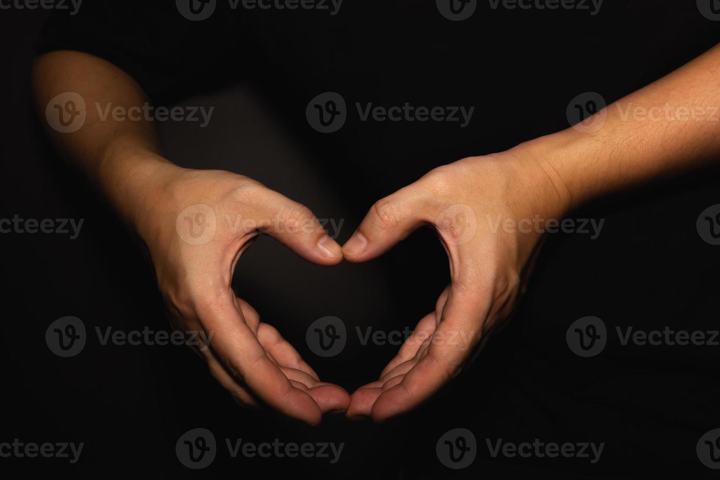 A man with a heart shaped hand on a black background photo