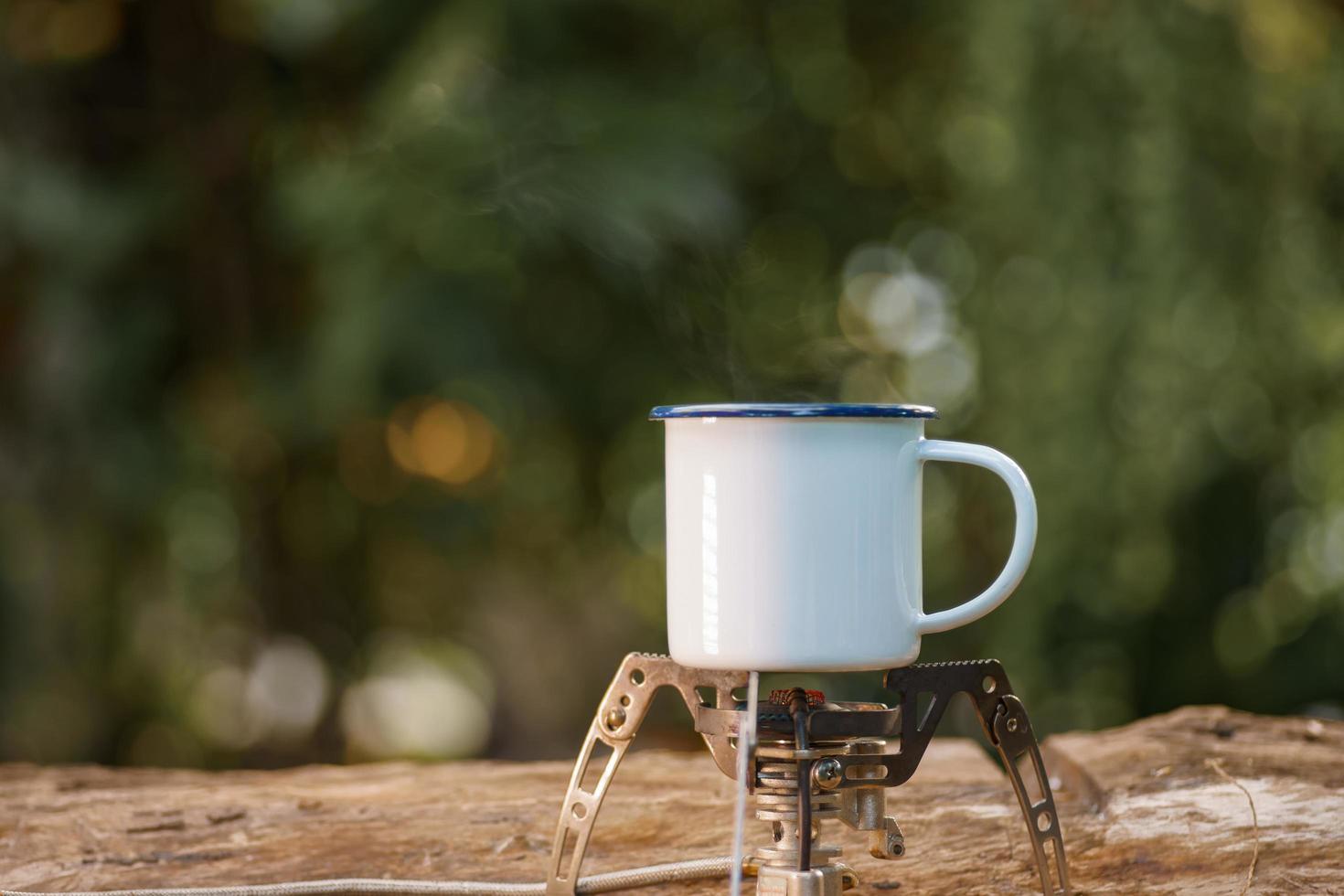 white enamel coffee mug on the gas stove green forest bokeh background.vintage style. photo