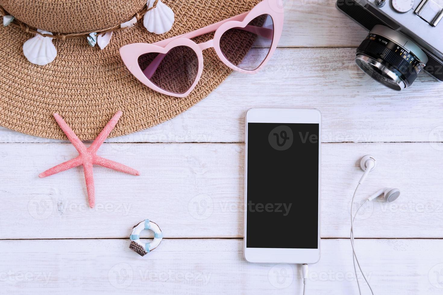 sombrero de playa con artículos de viaje y teléfono inteligente sobre fondo de madera blanca, concepto de vacaciones de verano foto