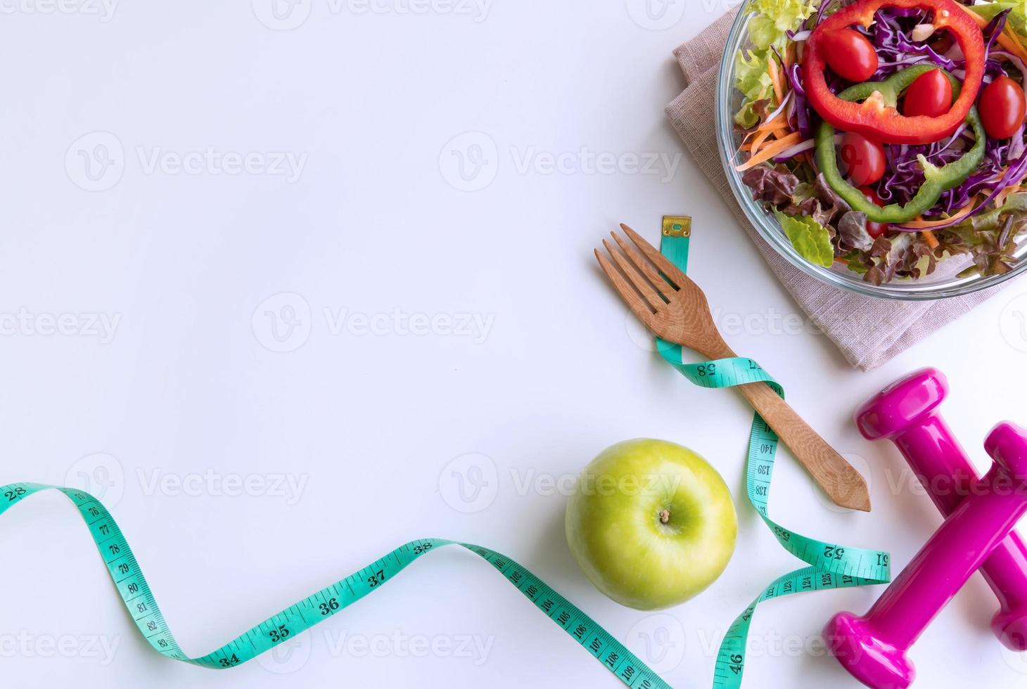 Fresh salad with green apple, dumbbell and measuring tape on white background. Diet, healthy eating concept photo