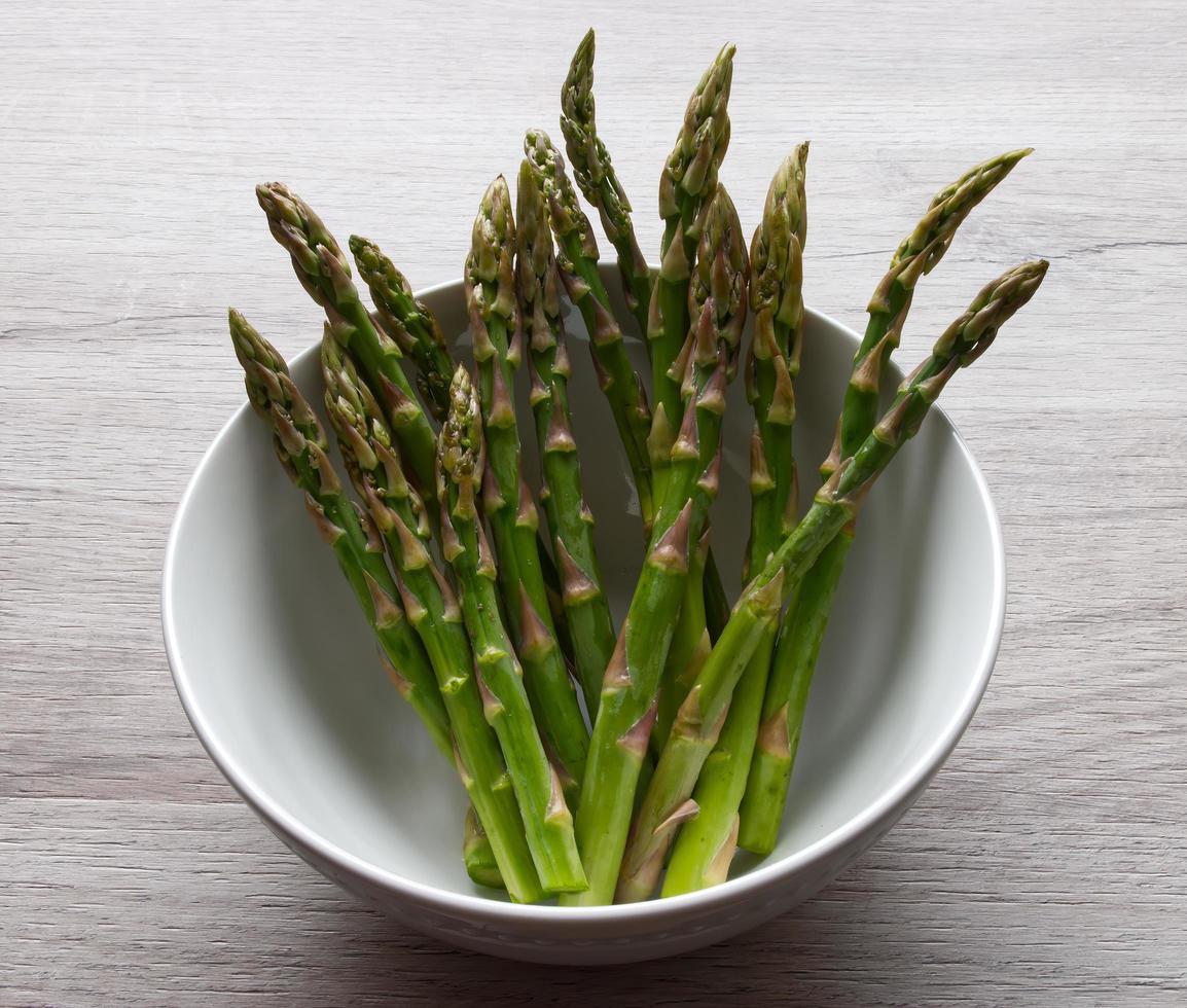 Fresh asparagus in a bowl isolated on wooden background photo