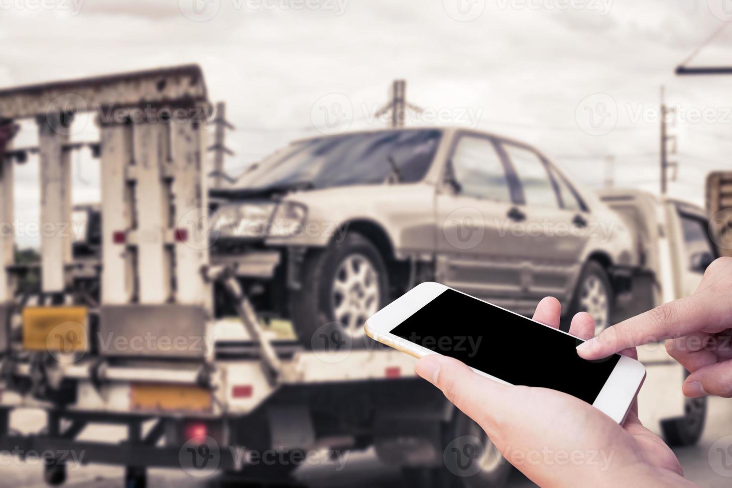 Hand using mobile smartphone for emergency roadside service with Broken car on tow truck after traffic accident background photo