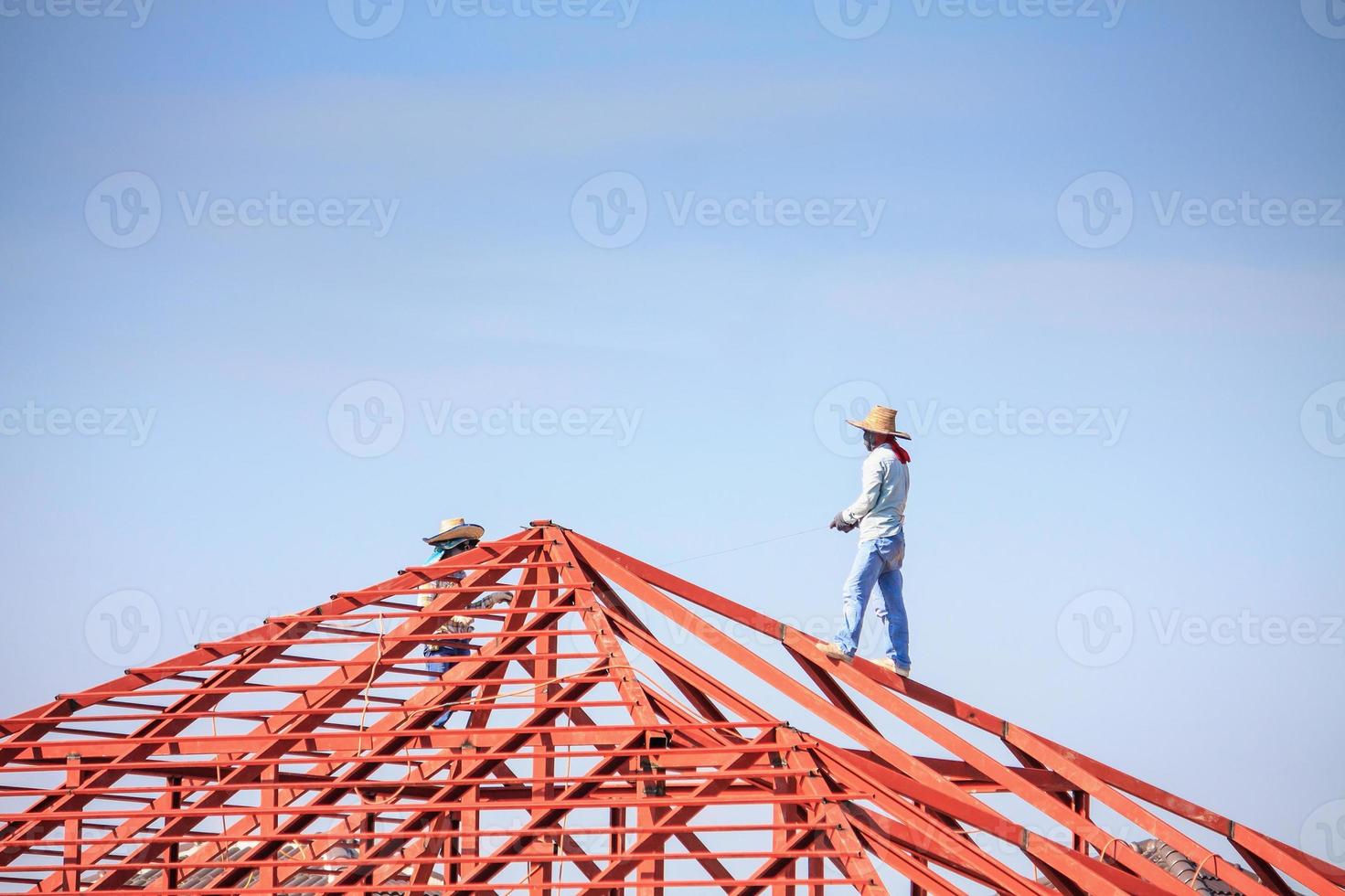 welder workers installing steel frame structure of the house roof at building construction site photo