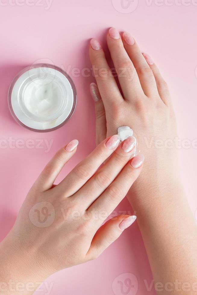 Nourishing cream and beautiful female hands on pink background. Skin care concept. Image for advertising and design. photo