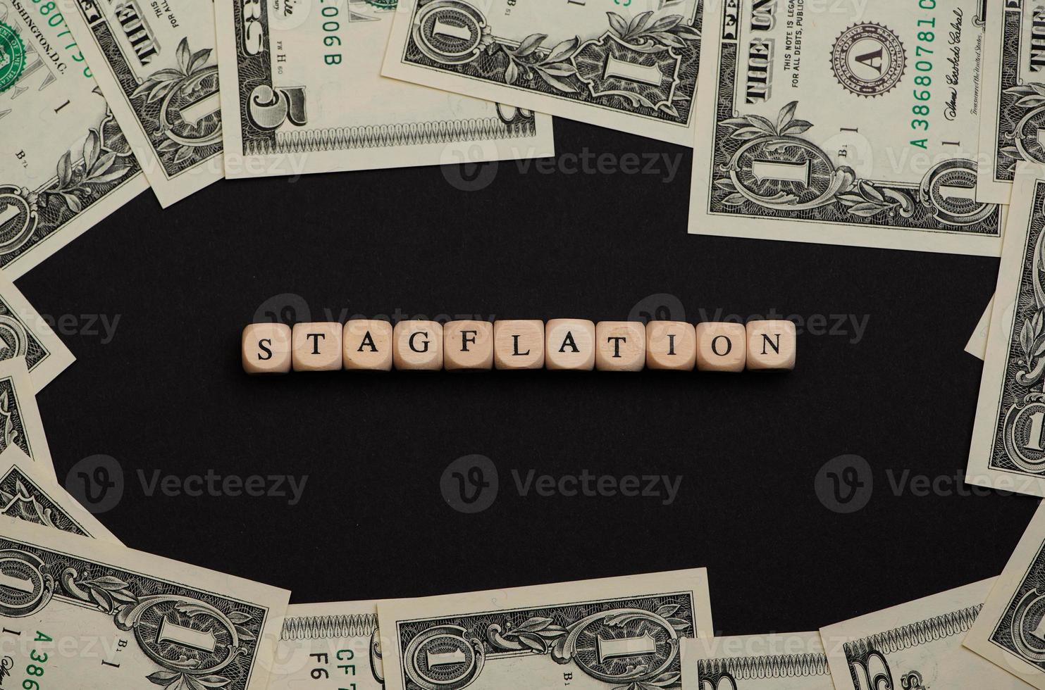 the word stagflation laid with wooden cubes on black background with Dollar banknotes around photo