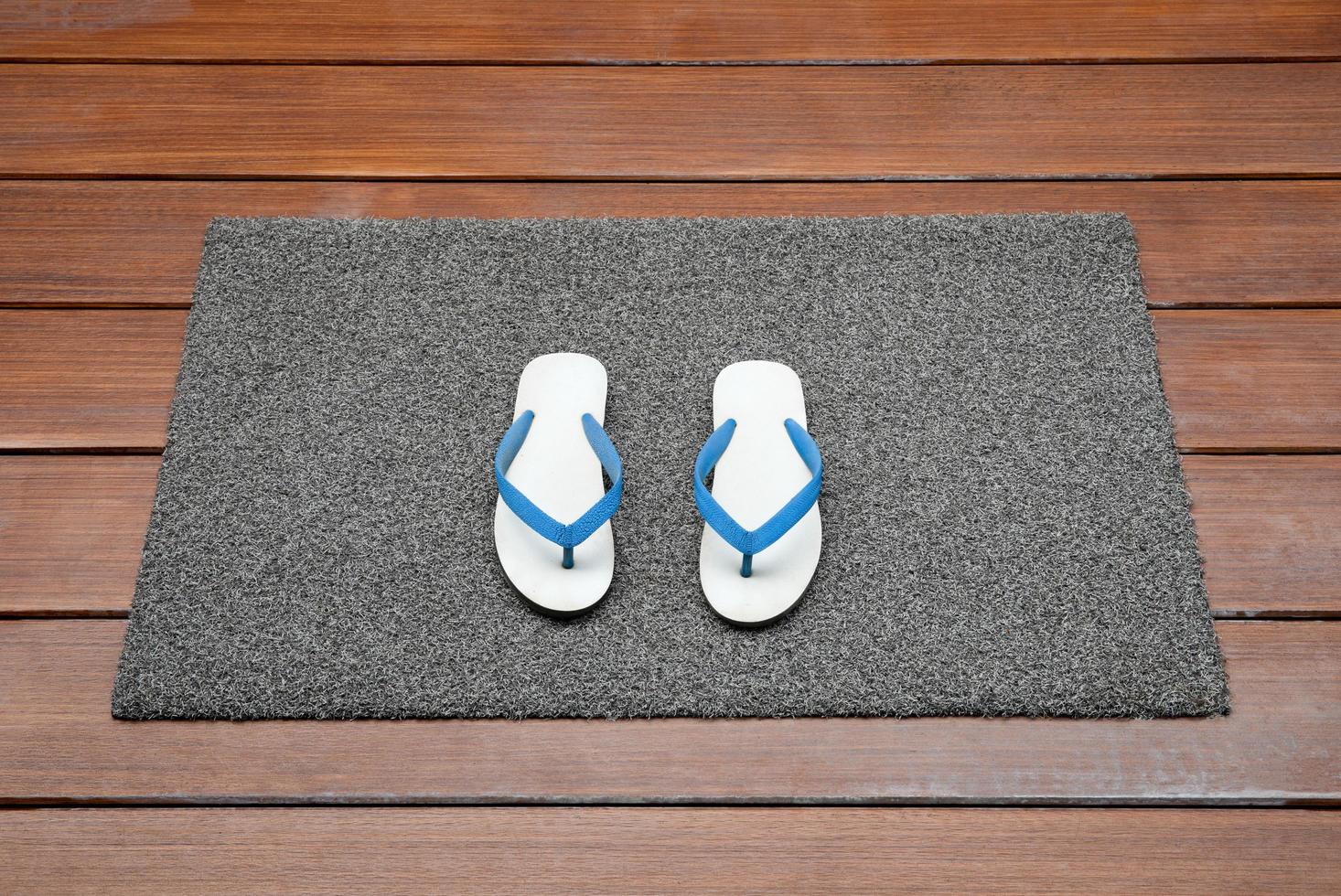 Dark gray doormat with white slippers on wooden floor photo