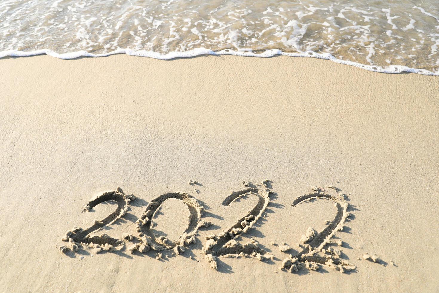 números 2022 año en la orilla del mar, escritos a mano en la arena en el fondo de la playa. foto